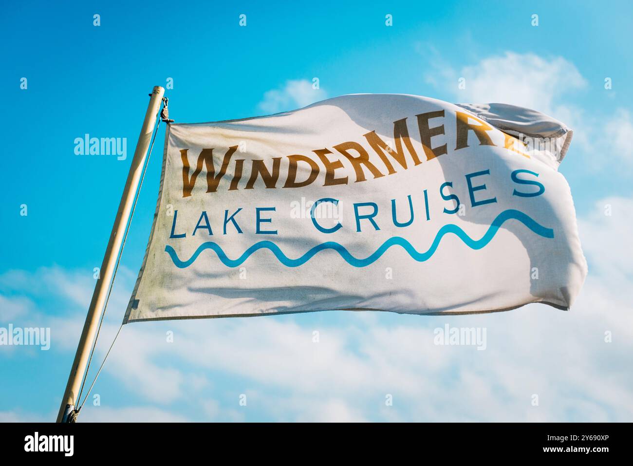 The Windermere Lake Cruises flag flutters in wind under a blue sky in the Lake District, showcasing a popular tourist activity in Cumbria, England. Stock Photo
