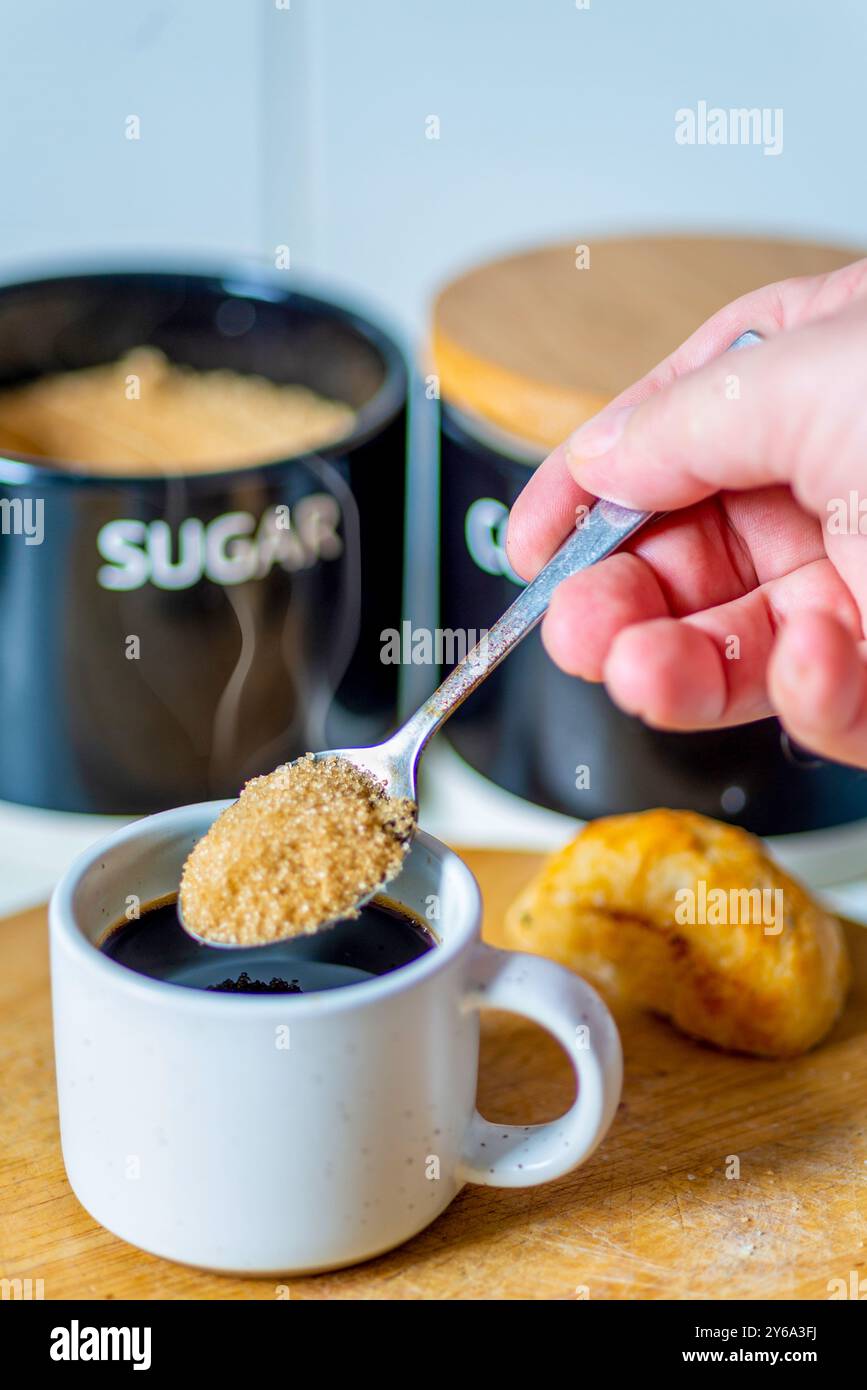 Freshly poured espresso,hot and ready to drink at breakfast,a silver spoon about to mix in brown sugar to sweeten,on a wood board, a bread roll,sugar Stock Photo