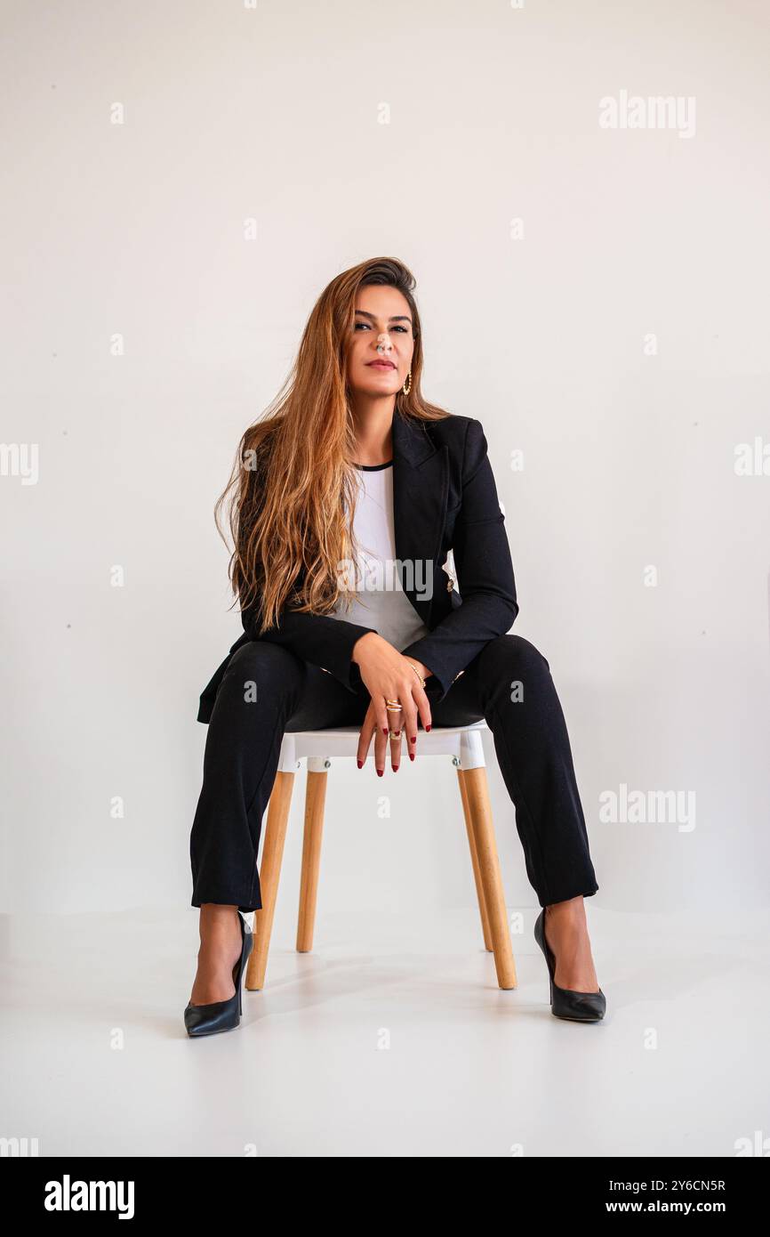 Confident young woman in a black suit sitting on a chair against a ...