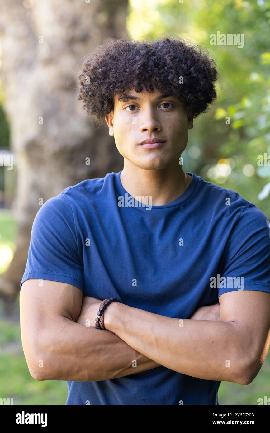 Man with curly hair standing outdoors with arms crossed, looking confident Stock Photo