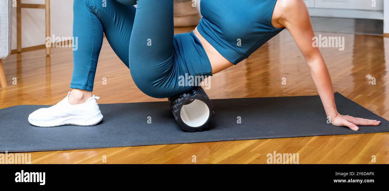Female athlete in sportswear is exercising with a foam roller on a yoga ...