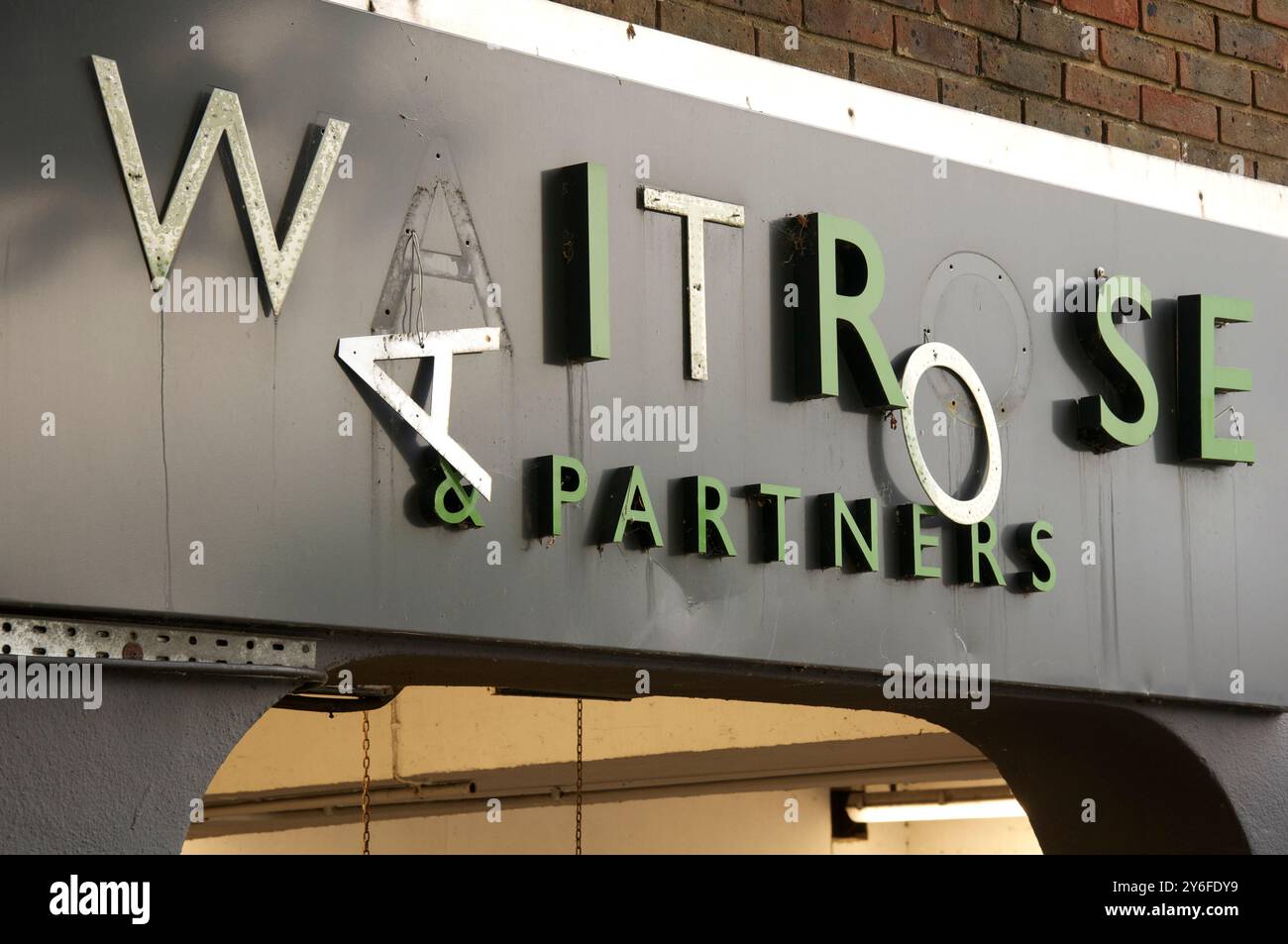 Broken and neglected Waitrose and Partners sign, falling apart with letters hanging off. Seen above the supermarket car park entrance. England, UK. Stock Photo