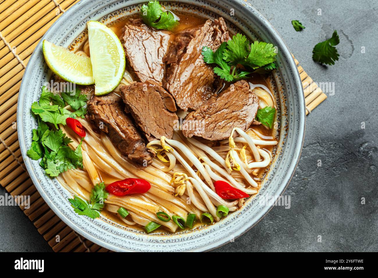 Pho Bo Vietnamese soup, bowl of fresh asian soup with rice noodle, beef, herbs, soy sprouts and chili on concrete background, top view. Asian cuisine, Stock Photo