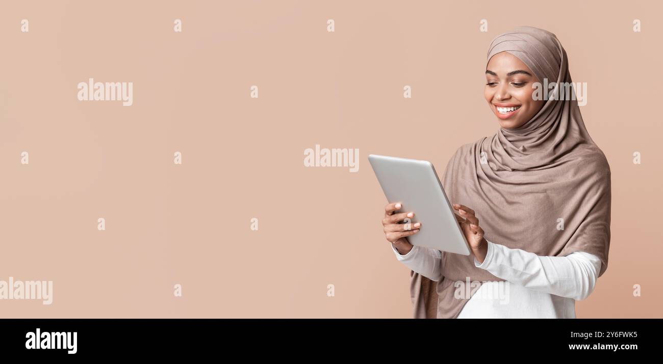 Portrait of smiling afro muslim girl in hijab using digital tablet ...