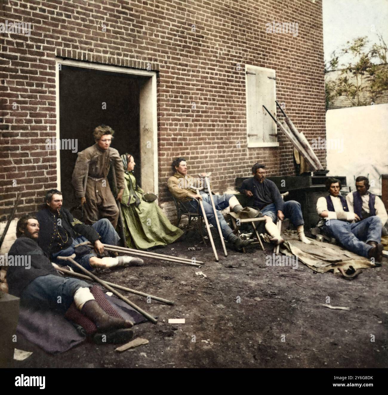 Created by James Gardner. Photograph shows soldiers outside a brick hospital building in Fredericksburg, Virginia, recovering from wounds received during the battles in the 'Wilderness campaign.' Woman seated in doorway is volunteer nurse Abby Hopper Gibbons from New York City. (Source: descendant Angela Schear, Oct. 2013).   Orinial text from the card accompanying the image:  Hospital at Fredericksburg, Virginia., May, 1864. This is one of the hospitals established by the Sanitary Commission, in Fredericksburg, Virginia during the Wilderness campaign in 1864. The wounded are from the Kearney' Stock Photo