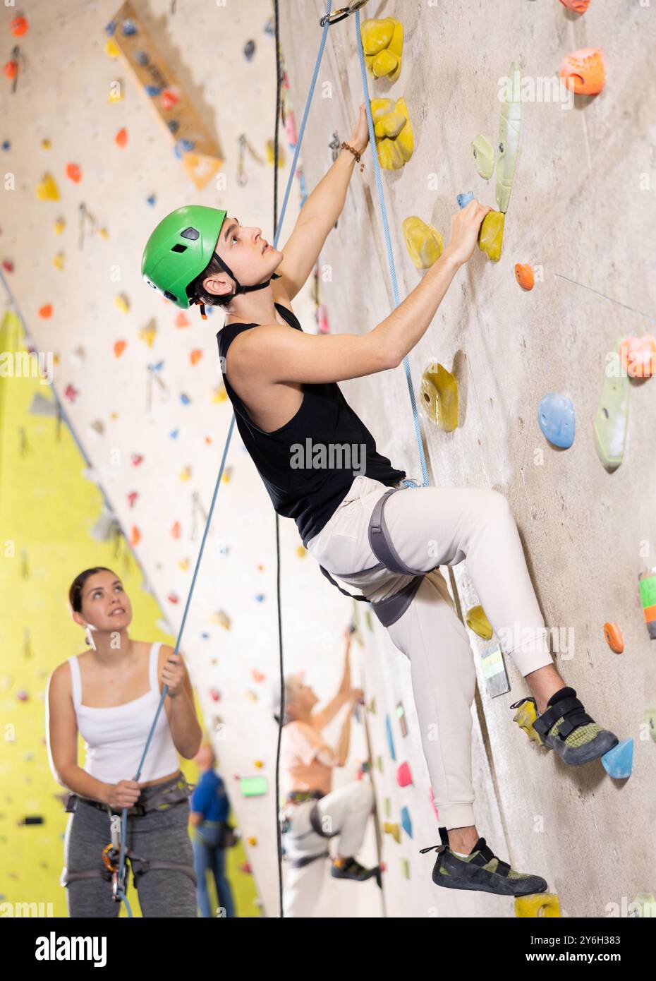 Determined young man in safety helmet doing his best at climbing artificial wall Stock Photo