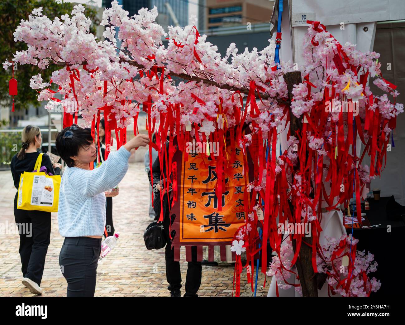 A female Chinese Reading good wishes written on Red Ribbons at Matchmaking Market Stall - Chinese Traditional Cultural Festival, Melbourne, Australia. Stock Photo