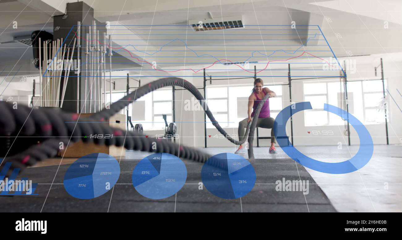 Fitness data analysis image over woman exercising with battle ropes in gym Stock Photo