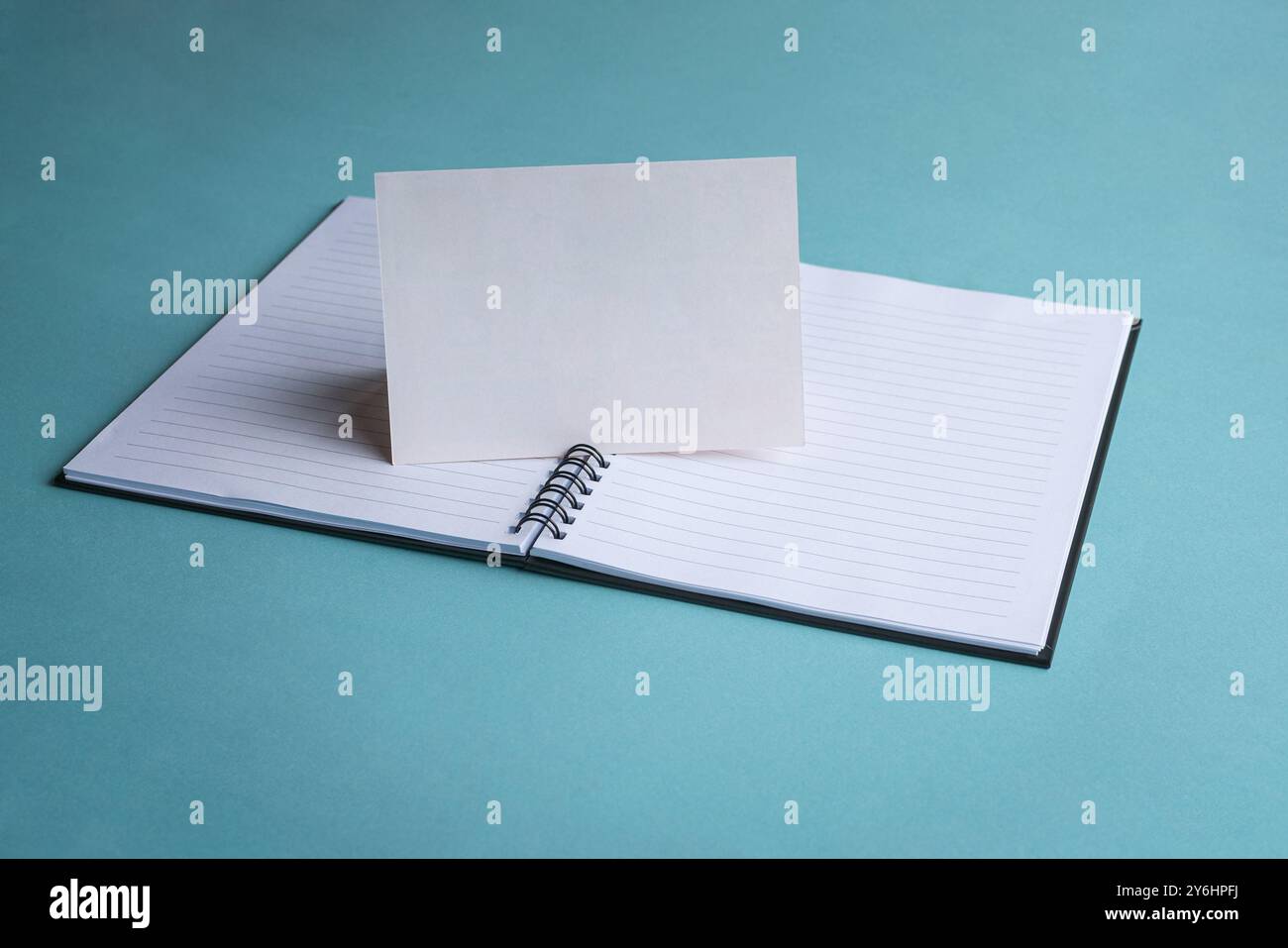 Blank white card on top of notepad and blue color table top. Stock Photo