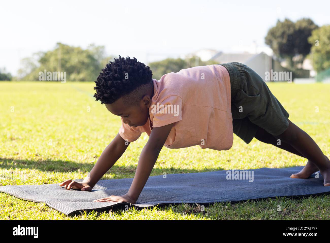 Practicing yoga, african american boy doing plank pose on yoga mat outdoors at school Stock Photo