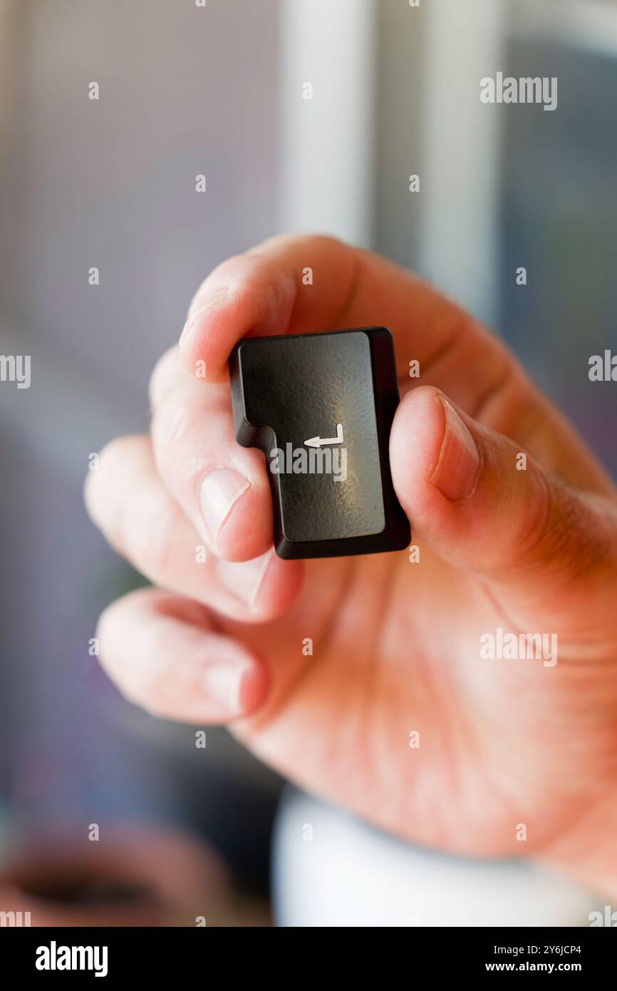 A hand holding a small black enter key out of the keyboard. Concept of control and precision, as the person is holding the key with a firm grip Stock Photo