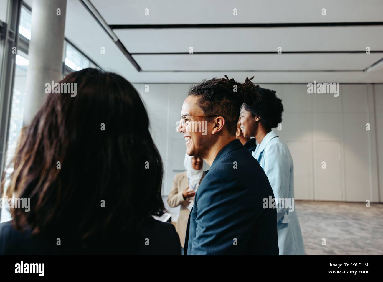 Young businessman with dreadlocks smiling while engaging with colleagues in a professional and happy work environment. Stock Photo