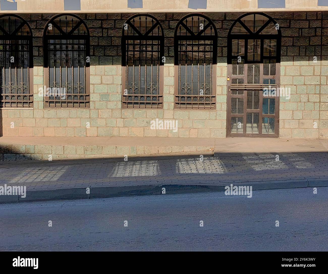 Morning Light and Shadows on Stone Wall Architecture with Door and Window Frames—Reflections on Pavement Floor Stock Photo