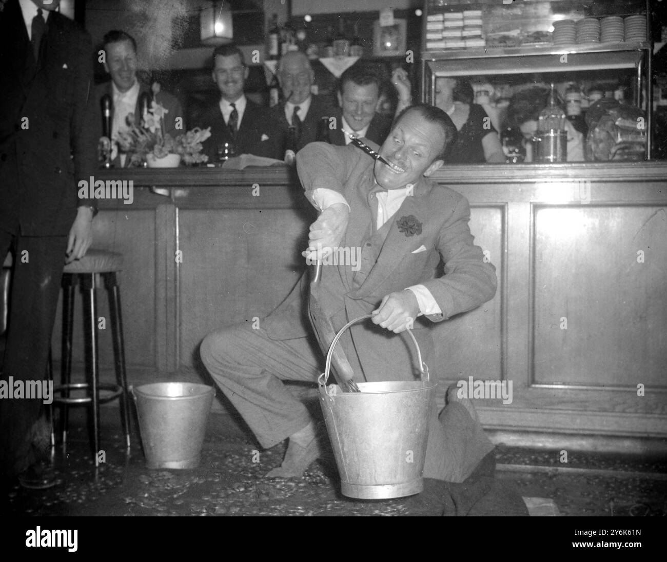 Manager and customers of Albany Hotel Albany Park Kent watch the English comic actor Terry Thomas do a humorous turn with a pail bucket and hand shovel 12 March 1958 Stock Photo