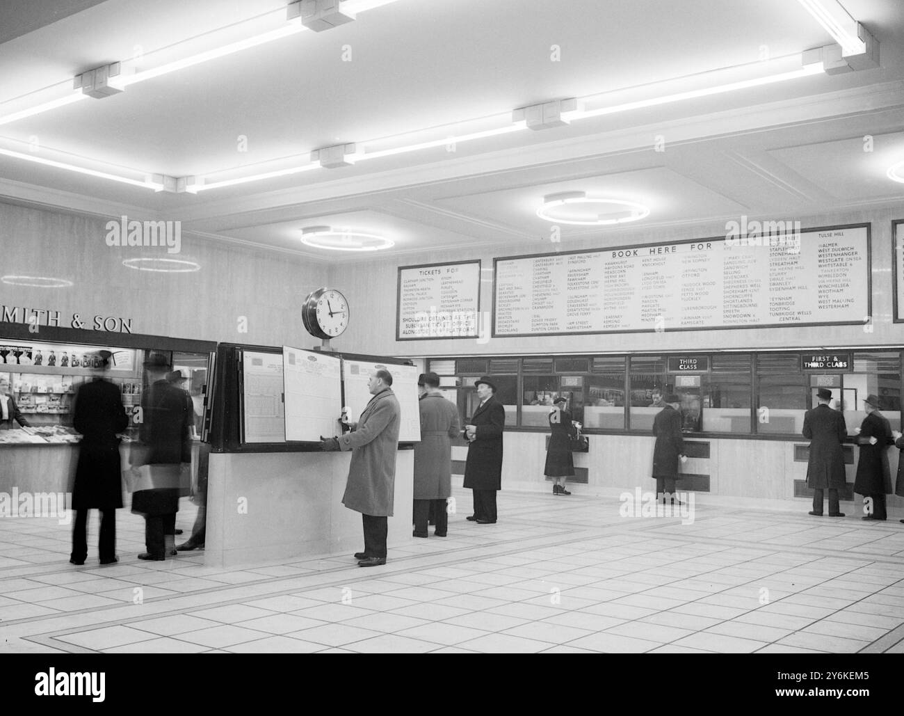 A view of the rebuilt Eastern Section Booking Hall at Victoria Station in London, showing the glass-fronted ticket office and passengers buying tickets.  Centrally-heated and lit with fluorescent lighting, of intermediate white and gold colours to give a warm and comfortable atmosphere, it contains bookstall, telephones and timetable stands. - 5th February 1951. ©TopFoto Stock Photo