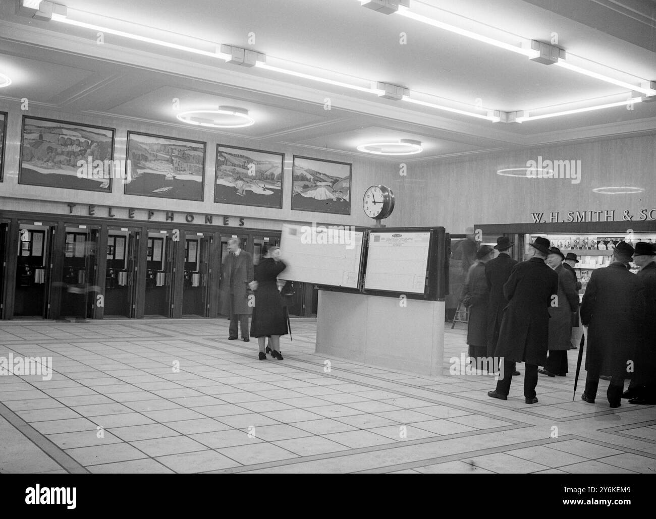 A view of the rebuilt Eastern Section Booking Hall at Victoria Station in London, showing the glass-fronted ticket office and passengers buying tickets.  Centrally-heated and lit with fluorescent lighting, of intermediate white and gold colours to give a warm and comfortable atmosphere, it contains bookstall, telephones and timetable stands. - 5th February 1951. ©TopFoto Stock Photo