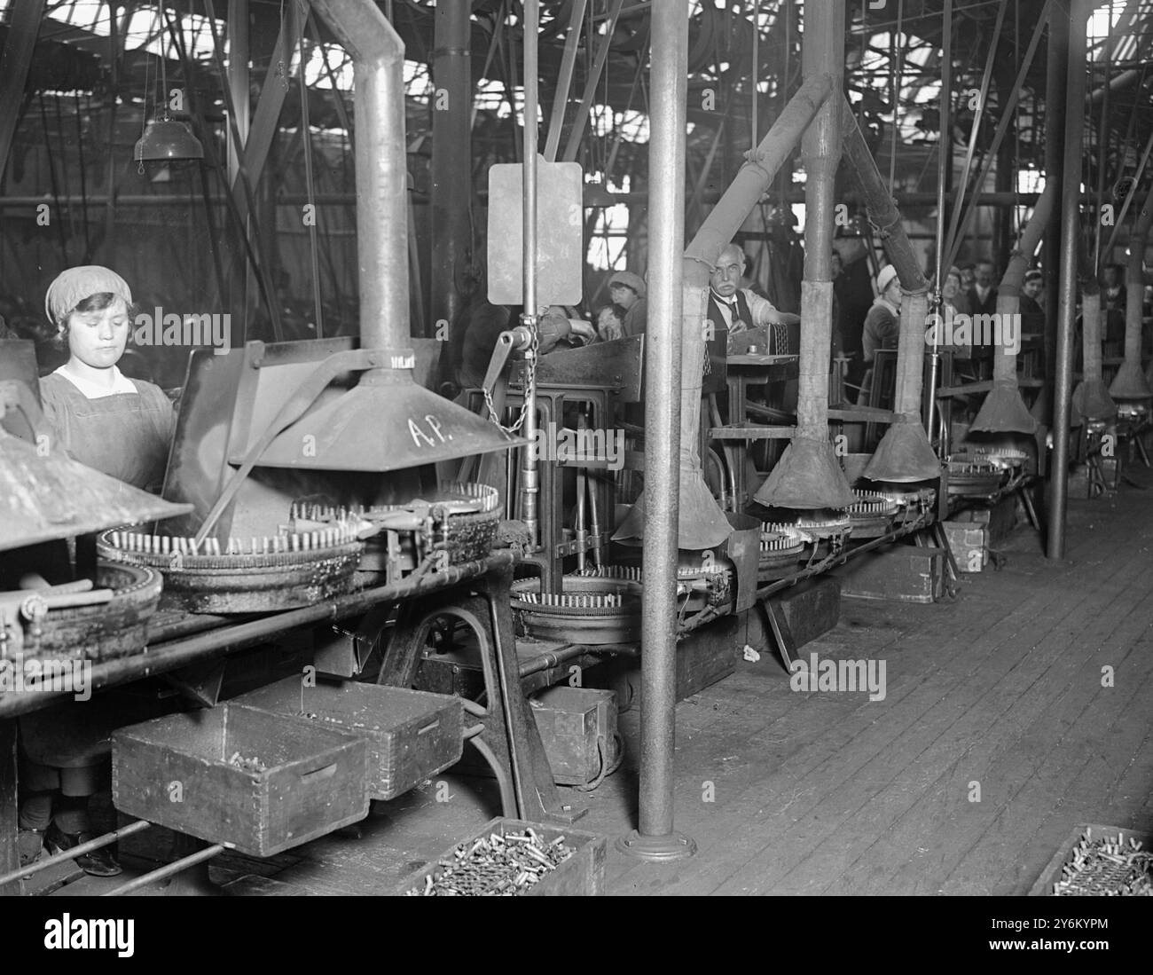 Easter at Woolwich, south-east London. Munitions work over the holiday. Boys, girls, women & men work on the machine which cuts the lead cores for bullets and forms and trims the bullets. In the cartridge tapering and pressing room. 29 March 1918 Stock Photo