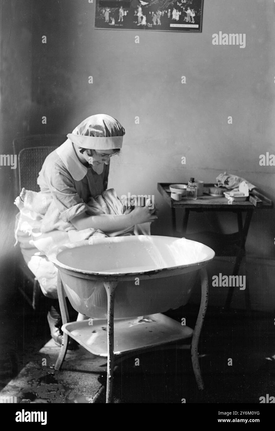 Order of the bath.  Nurse soaps baby's head, using bath square and pure curd soap. She rinses the little scalp thoroughly to prevent scurf. Holding the head well over the bath in the safe crook of her left arm.  for leech's leach's (?) childrens book Stock Photo