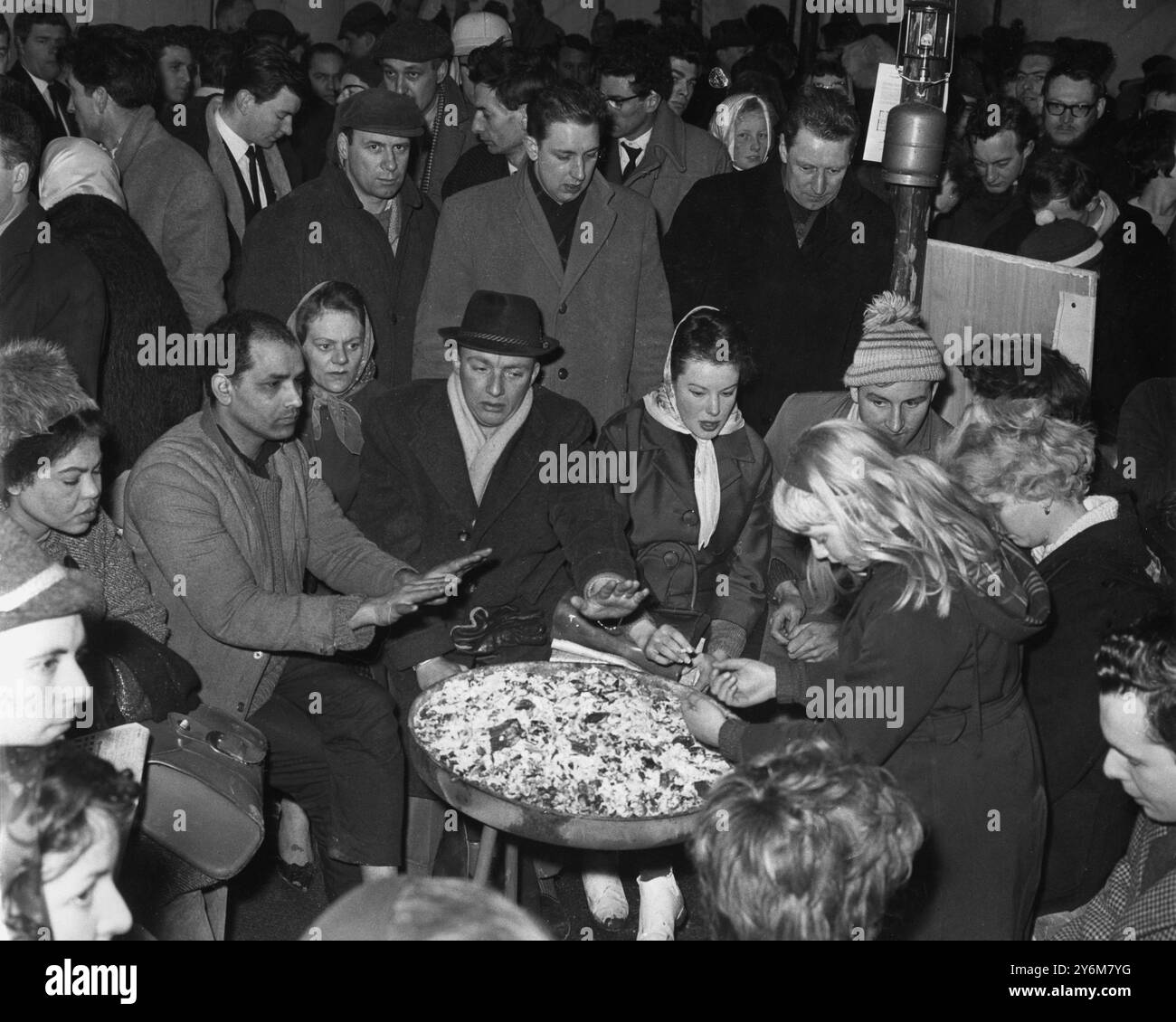 Home-seekers who had camped in cars and tents through days and nights of wind, rain and bitter cold spend the last few minutes of their long wait warming themselves around a brazier at a Sunbury on Thames, Middlesex, building site.  They were in a queue which formed to buy 152 homes yet to be built.  The contractors' office was soon opening so that prospective purchaser could sign on and pay their £50 deposits. - 4th April 1964. ©TopFoto Stock Photo