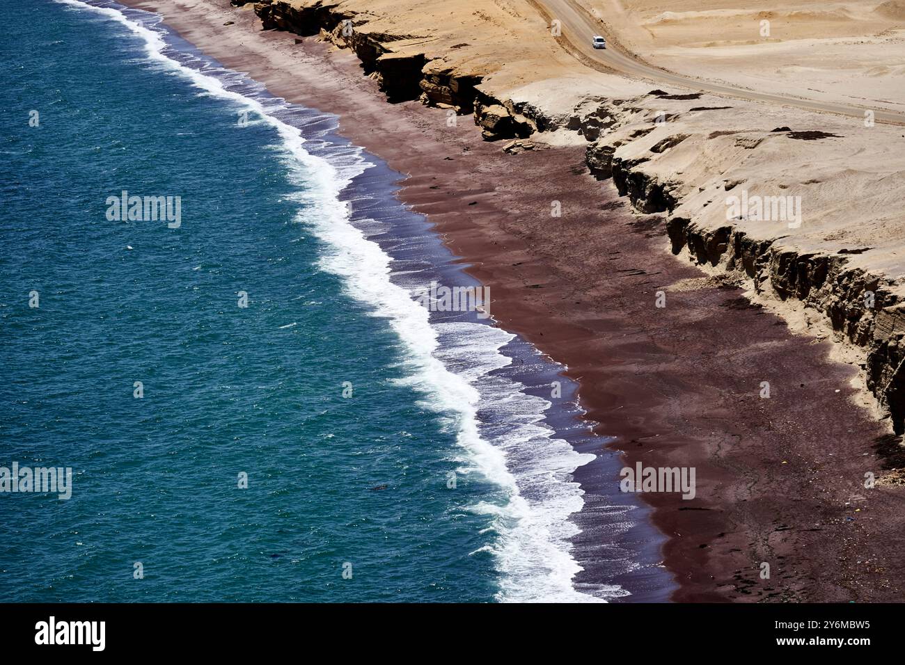 A stunning aerial view of Paracas beach, showcasing the contrast between the blue ocean waves and dramatic desert cliffs under a clear sky. Stock Photo