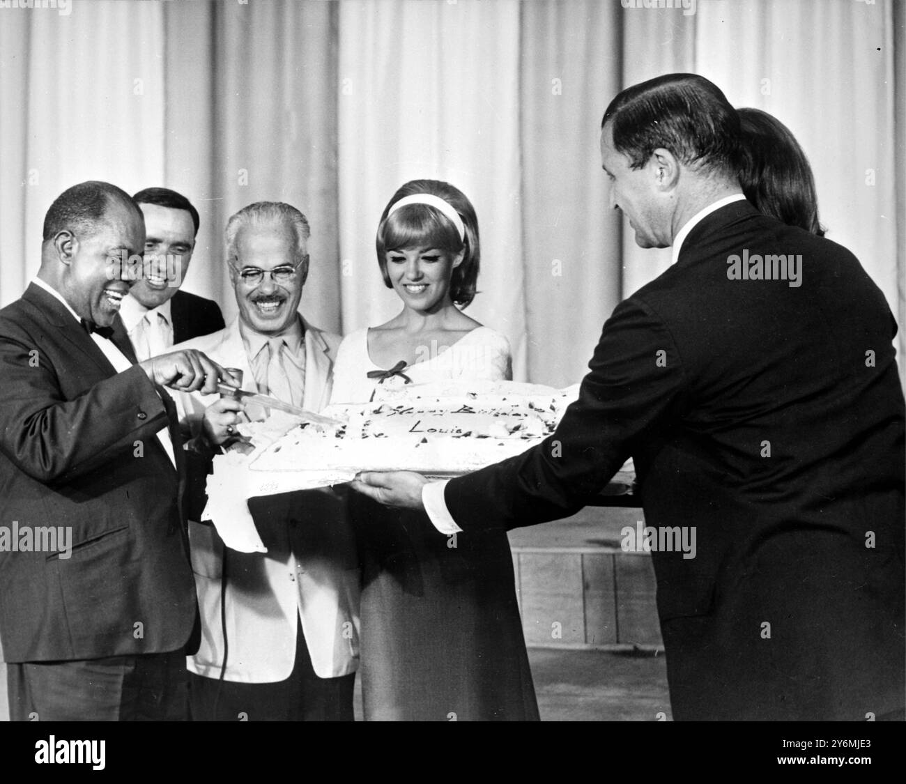Atlantic City, U.S.A: Louis 'Satchmo' Armstong and a giant cake for his 65th birthday  and he did not resist. He gave a TV interview which his mouth full of icing, on the basis that for once he wouldn't need to blow his own trumpet. Louis has just returned to America after a visit to Europe including a sell out concert in Budapest. 14 July 1965 Stock Photo