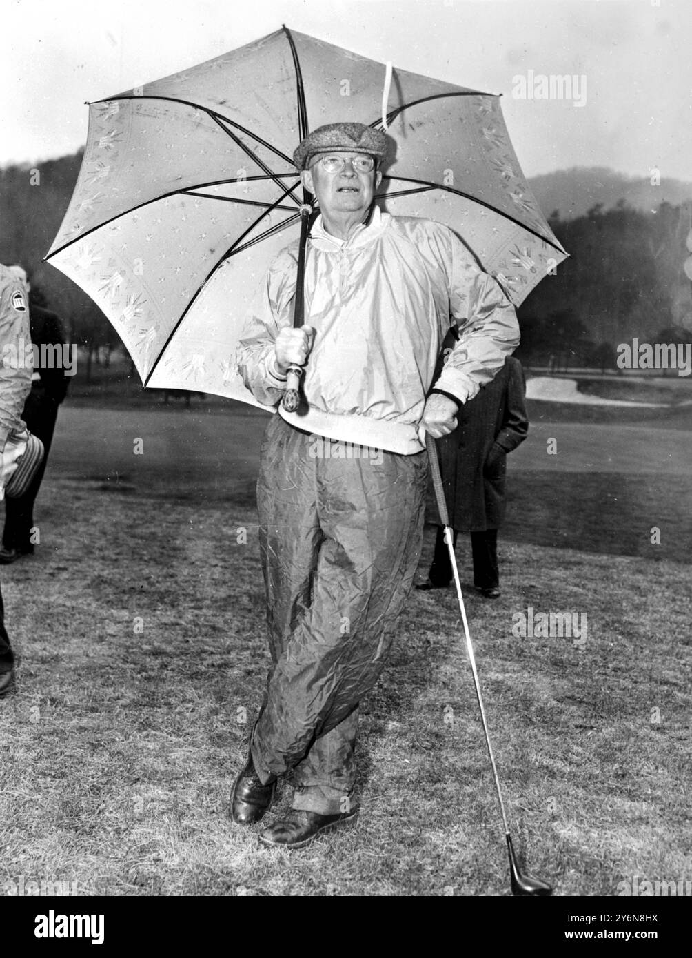 White Sulphur springs, West Virginia: Wearing red rain pants President Eisenhower takes shelter under an umbrella during a shower while  while enjoying a round of golf at the green brier Hotel in White Sulphur Springs. He played with the Greenbrier pro, Sammy Snead. Presdeint Eisenhower was meeting Canadian Prime Minister St Laurent and Mexico's President Cortines. 29 March 1956 Stock Photo