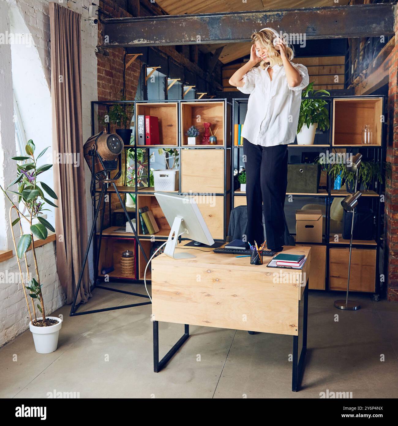 Woman stands on top of her desk, listening music, completely ...