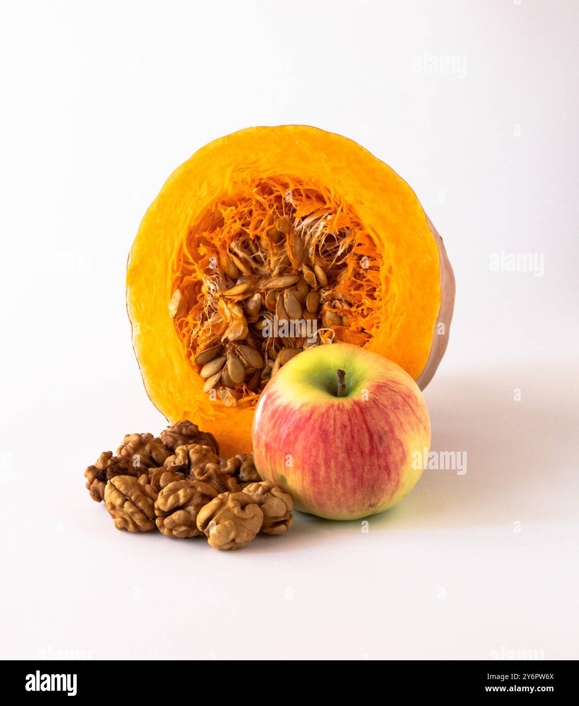 Cut pumpkin with seeds inside, apple, walnut kernels on a white background. Stock Photo