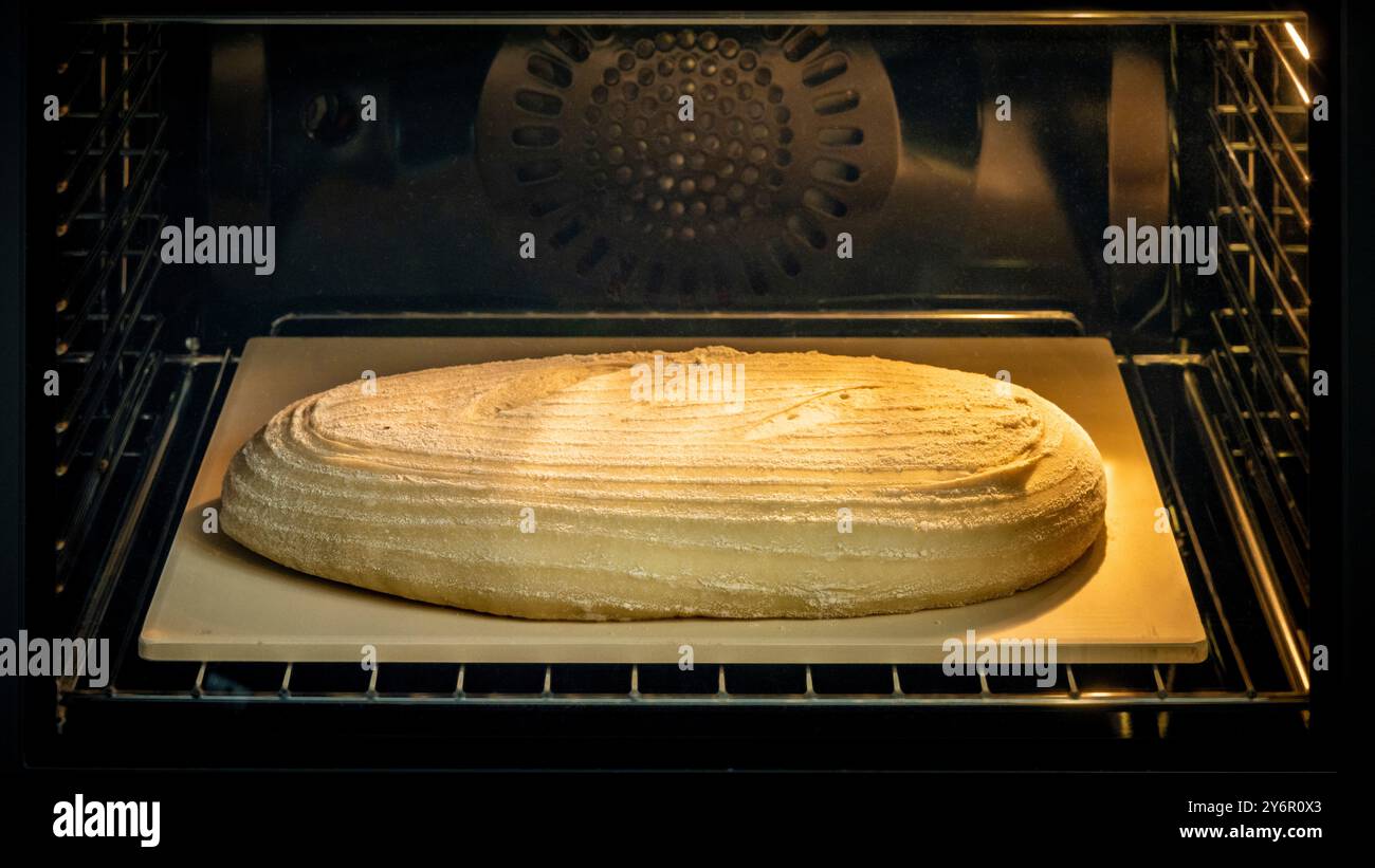 Oval-shaped bread dough on a baking stone seen through the oven door as it cooks. Timelapse 2 of a sequence of 5 Stock Photo