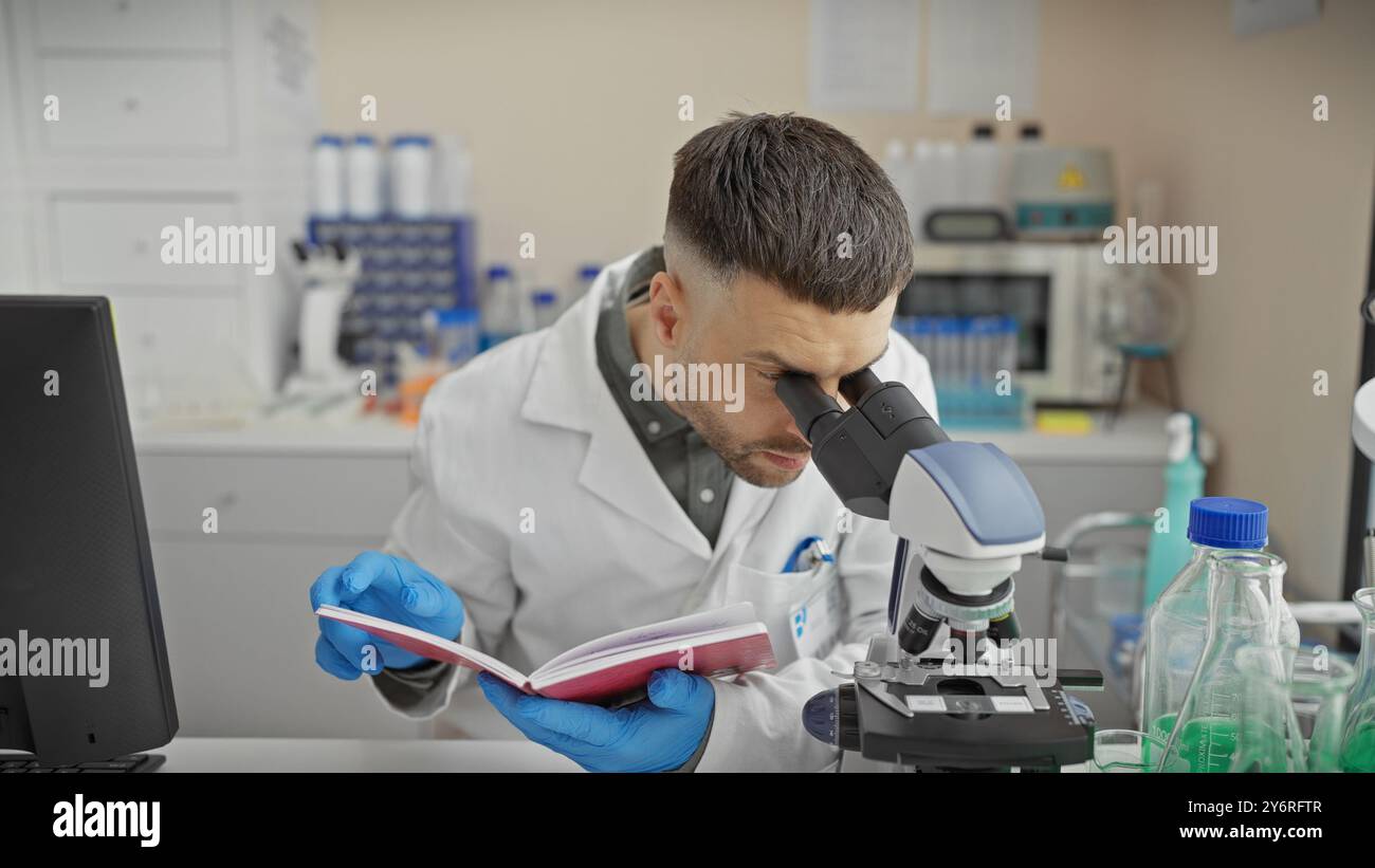 A young bearded man studies specimens under a microscope in an equipped laboratory setting. Stock Photo