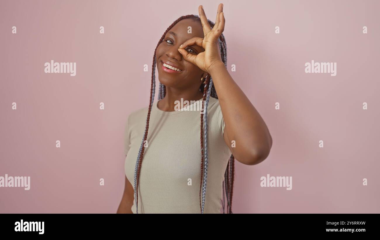 A smiling african woman with braids gestures playfully against a pink ...