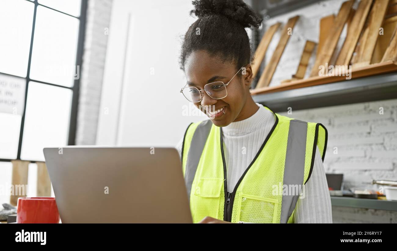 African woman in safety vest using laptop in a modern carpentry workshop Stock Photo