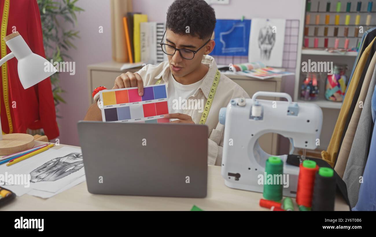 A young man compares fabric colors during a video call in a tailor shop surrounded by sewing equipment. Stock Photo