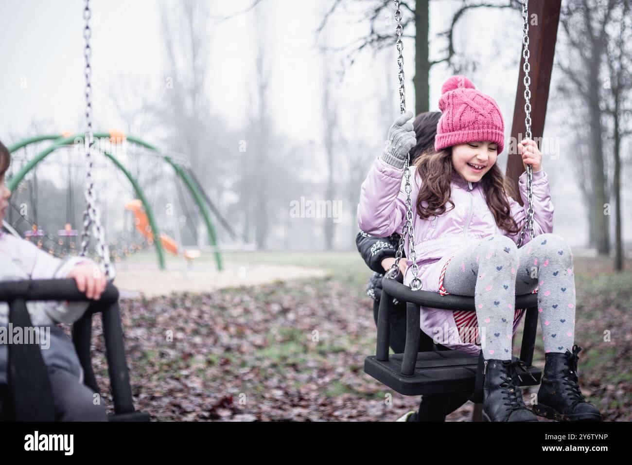 one smiling girl sitting on the swing at children playground on a foggy ...