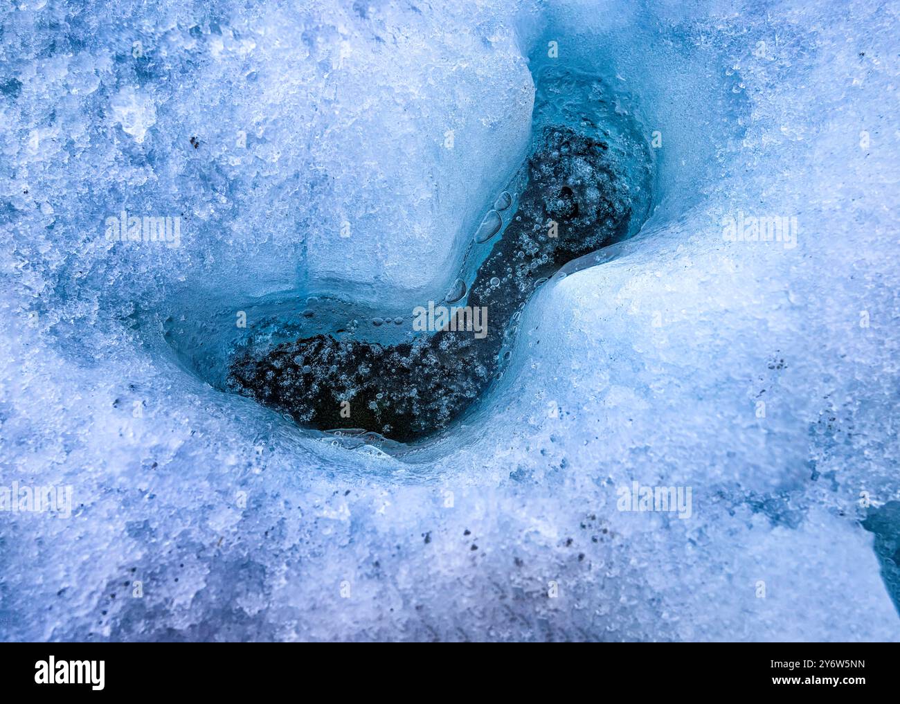 Air bubbles lie trapped in water under a thin layer of ice in a hole in the Glacial blue ice of the Matanuska Glacier Stock Photo