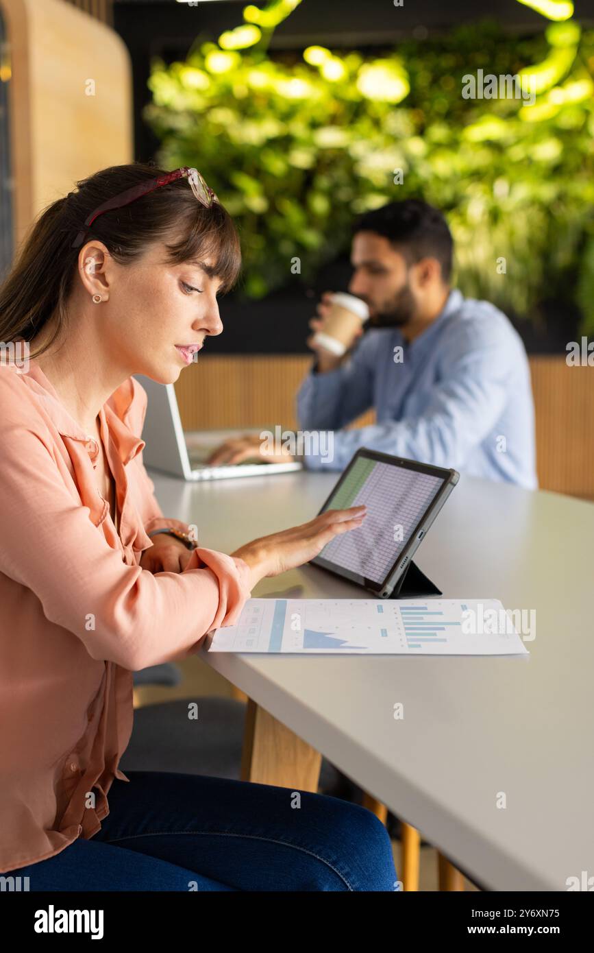 Using tablet for work, woman analyzing data while african american man working on laptop Stock Photo