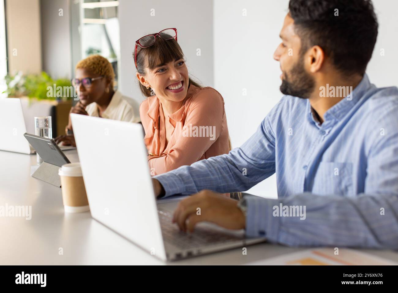 Working in office, colleagues discussing project using laptops and tablet, smiling Stock Photo