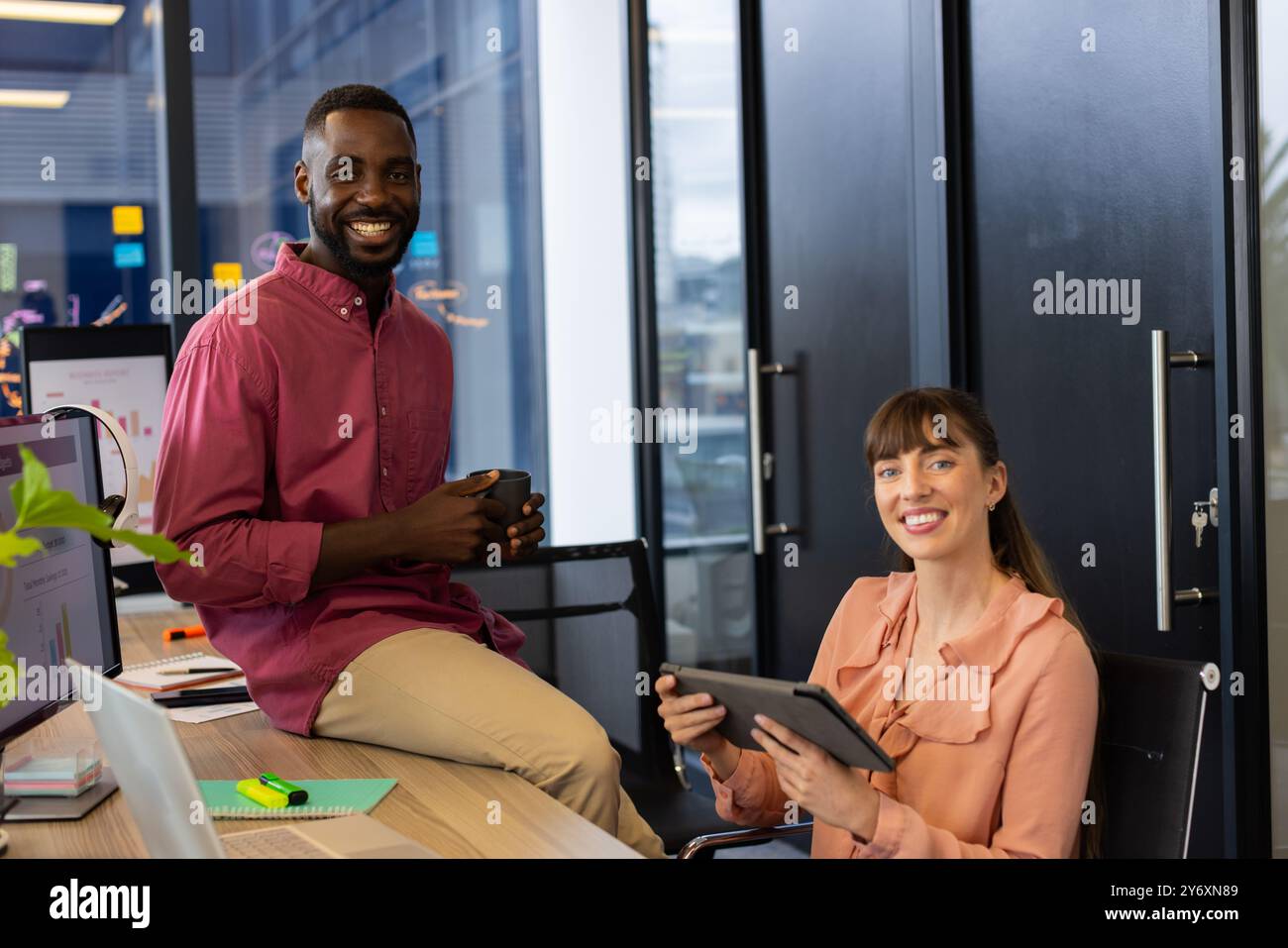 Collaborating on project, smiling colleagues in office using tablet and holding coffee Stock Photo