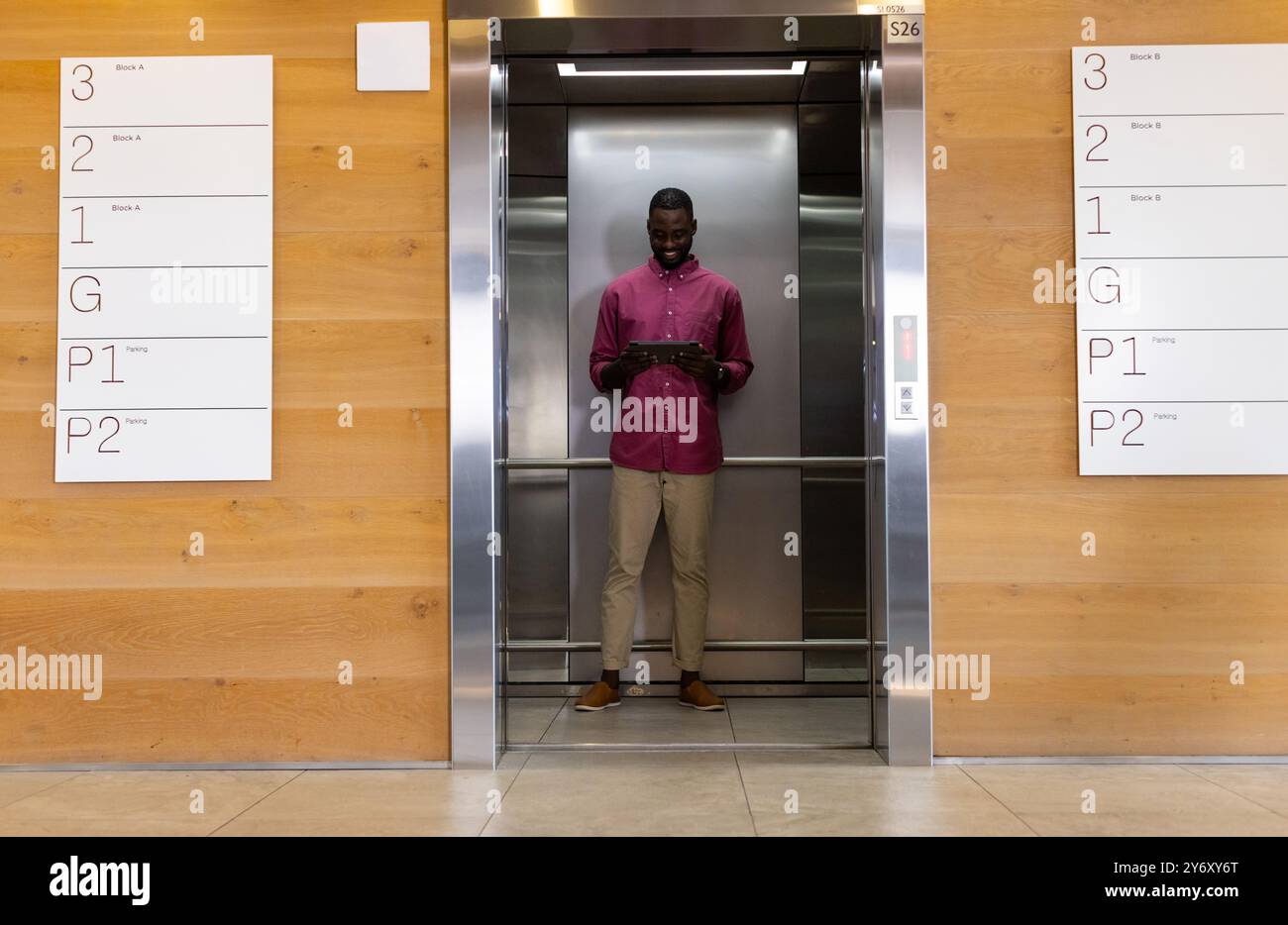 Standing in elevator, man using tablet and smiling, modern office building Stock Photo