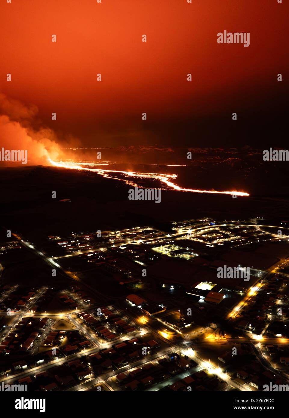Aerial view of a volcanic eruption with flowing lava near a city at ...