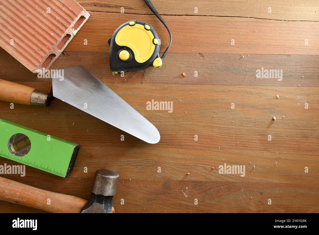 Construction tools such as trowel, level, tape measure, hammer and brick on wooden plank. Top view. Stock Photo