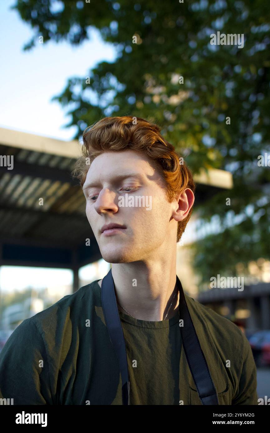 Young man with curly red hair gazing thoughtfully outdoors Stock Photo