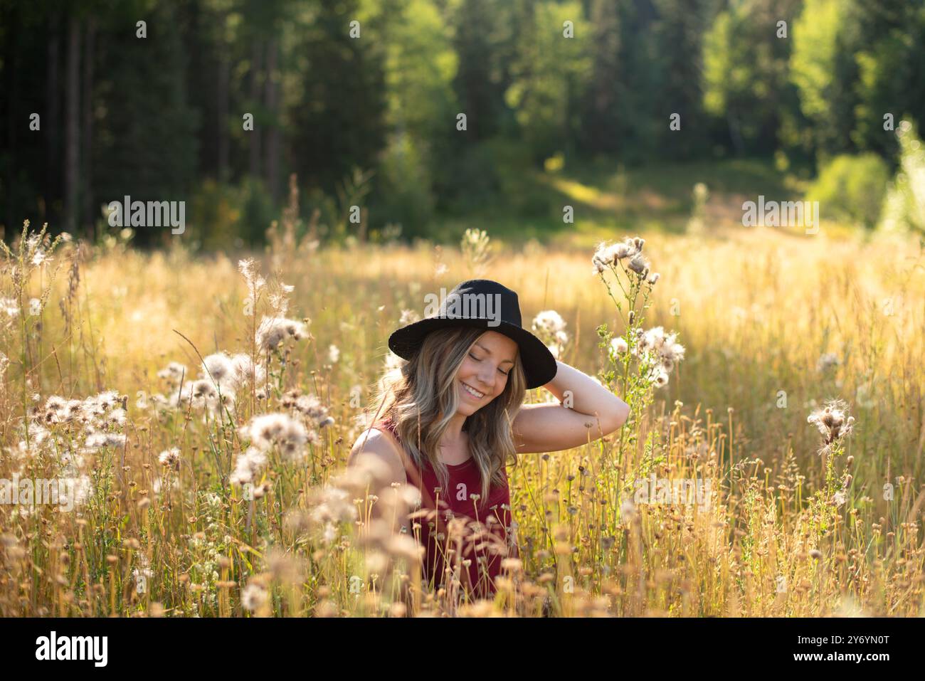 Woman sitting in grassy autumn meadow smiling in the sunshine Stock Photo