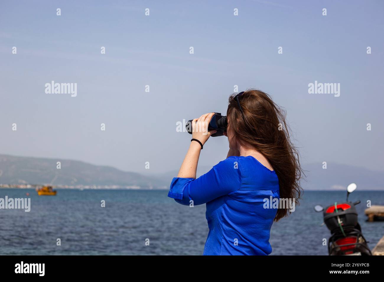 Young woman with long hair is looking through binoculars at the sea ...