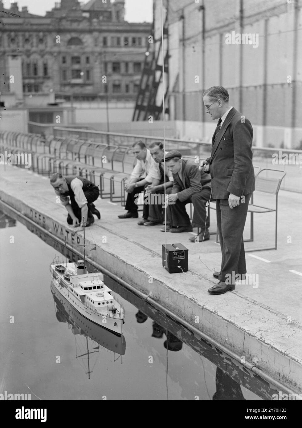 SIX FOOT YACHT MAY CROSS CHANNEL UNDER RADIO CONTROLL   Seen going through a test at the Oasis Swimming pool in Holborn , London , is a model Yacht six feet long which may cross the English Channel under radio control .  It was designed by Mr . H.W. EASTHAUGH of Shepperton , Middlesex , a Civil Servant interested in Wireless Control , who is seen ( on right ) directing the model by means of the radio unit .   During the attempt to navigate the Yacht across the channel - which is to be made this year - the yacht will be controlled from a boat which can operate at a range of three miles .  There Stock Photo