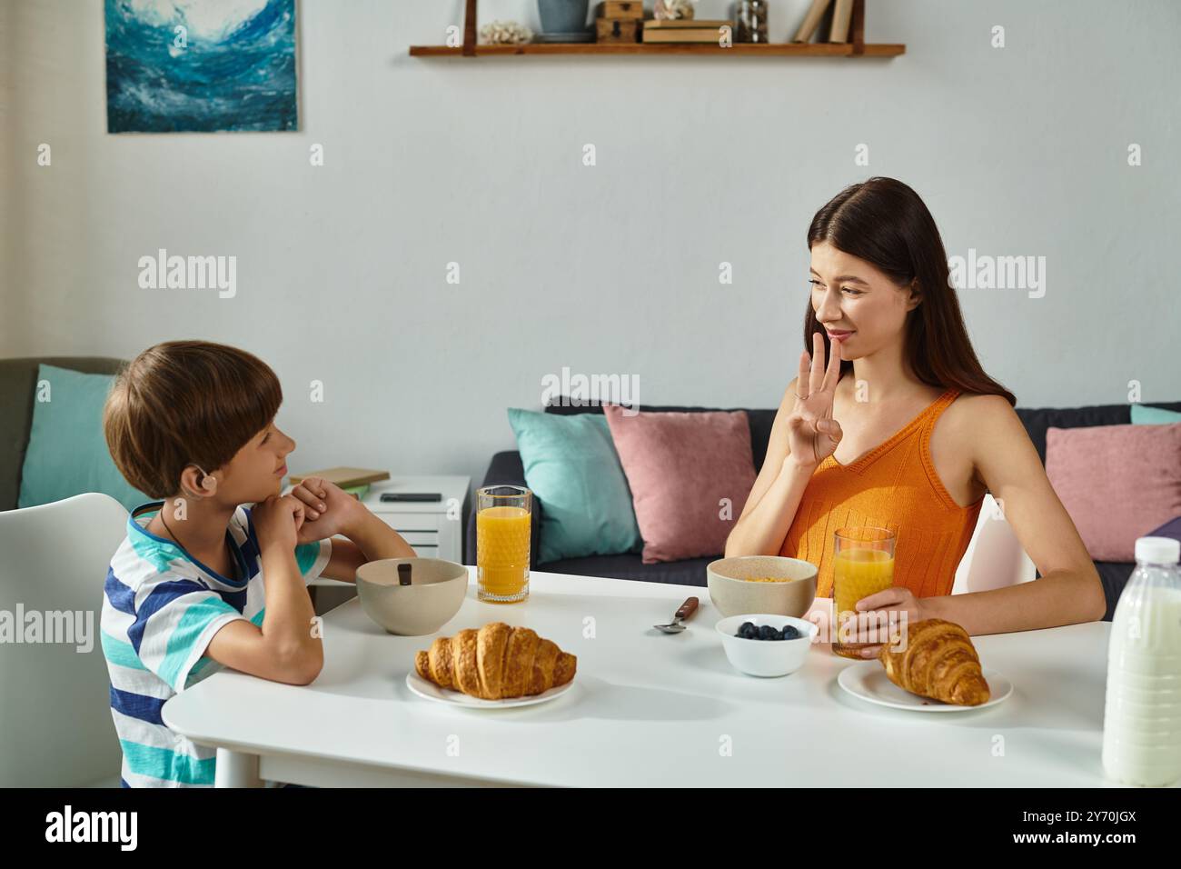 A boy with hearing impairment shares breakfast with his mother using sign language. Stock Photo