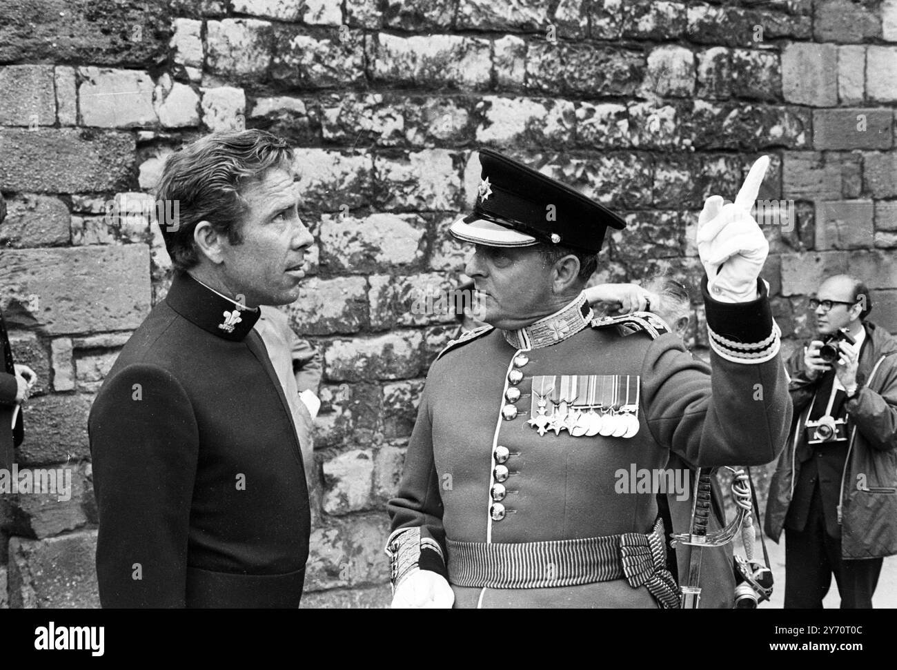 Caernarvon , Wales :  Even the usually gaily-dressed Lord Snowdon is in full uniform for this afternoons , investiture ceremony .  Dressed in the full regalia of Constable of Caernavon Castle he talks with Colonel C H Jaeger as he watches guests arrive from the Investiture of the Prince of Wales .  Two features of the Earl 's unifom are the morning style tail from his jacket and two tassels hanging from the side of his wide belt .1 July 1969 Stock Photo
