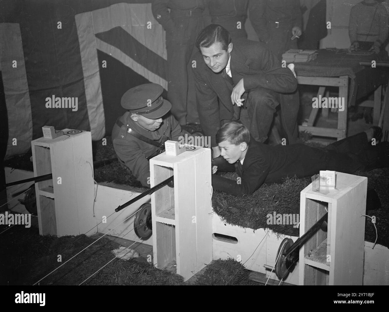 DEREK ON THE RANGE   J . Arthur Rank film star , DEREK BOND , watched his step-son , LARRY D'EATH , aged 13 , trying his hand on the Army Cadets Rifle Range , one of the many attractions at this year's schoolboy's Own Exhibition'' at the New Horticultural Hall , Westminster , London .     3 January 1949 Stock Photo