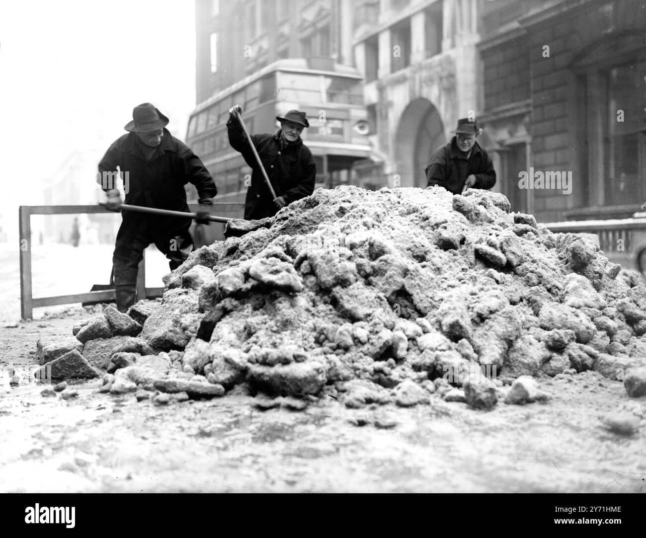 Westminster tackles snow in a big way.    A big snow clearance campaign has been started by Westminster City Council. They have a fleet of lorries removing snow from the streets to strategically located drains, where the snow is dumped. Main streets are being cleared first, less important ones will be dealt with afterwards - unless a thaw sets in. Photo shows: Wesminster Council employees shovelling a mountain of snow down a drain in Pall Mall. 8 March 1947 Stock Photo