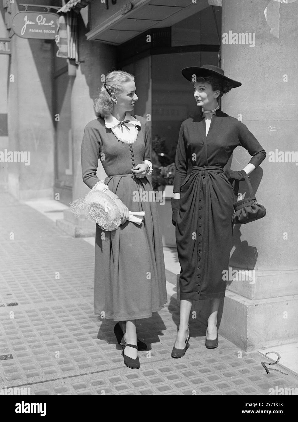 'FOR HOME AND AWAY' Opened by Mr. Leif Egeland , High commissioner for South Africa, at Dorland House , London , was a new display of home and export fabrics by British manufacturers, in jersey wool .  Picture shows:-  ' Black and Blue '-The model on right wears an exquisite black afternoon dress, made from fine wool jersey. It's pencil-slim skirt is draped at the front, with a prim bodice. Midnight blue is chosen by her companion for a wool jersey afternoon dress, with a full skirt and white silk , pique cuffs and gimp  April 29 1948 Stock Photo